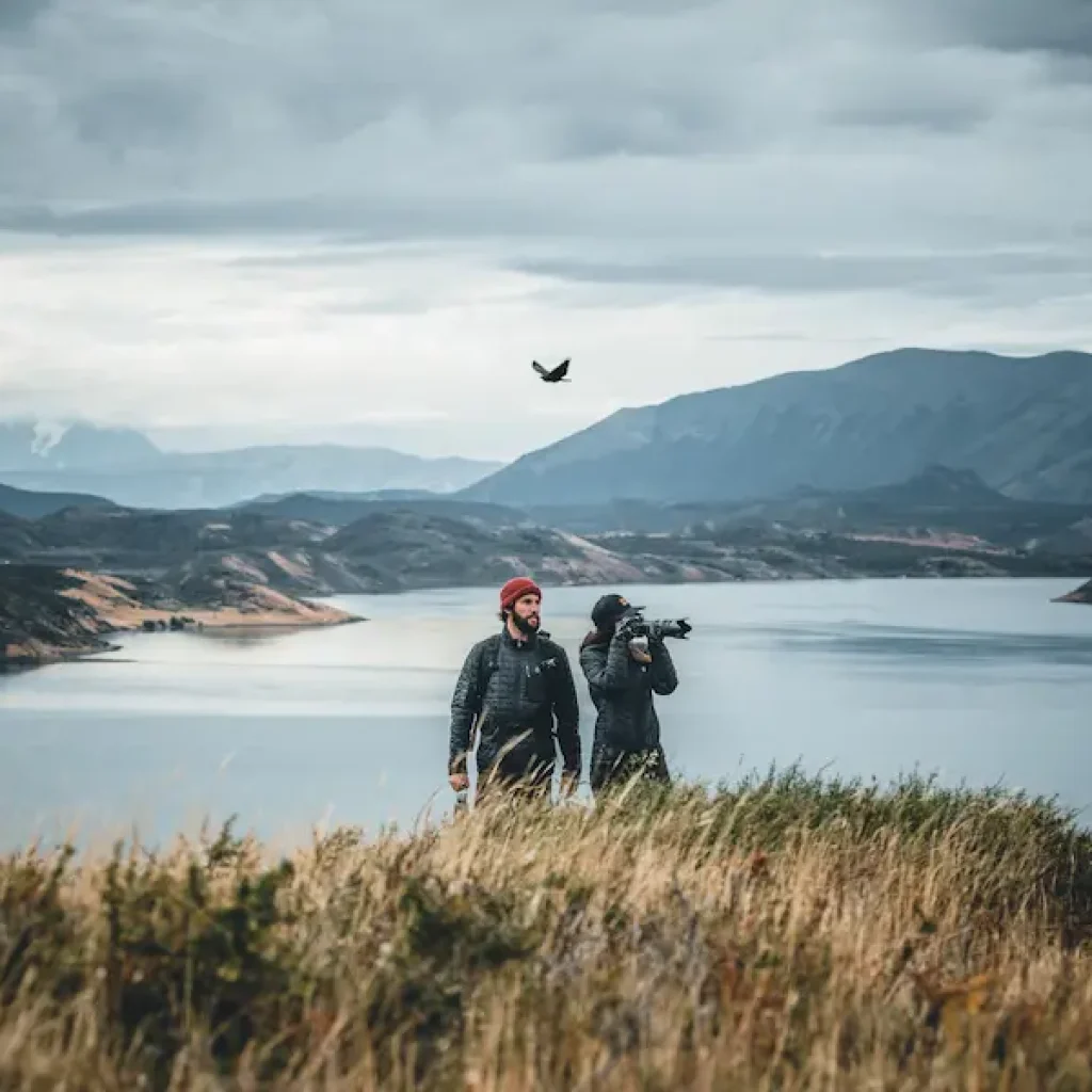 Dos viajeros sacan fotos del paisaje mientras un pájaro planea grácilmente sobre ellos.