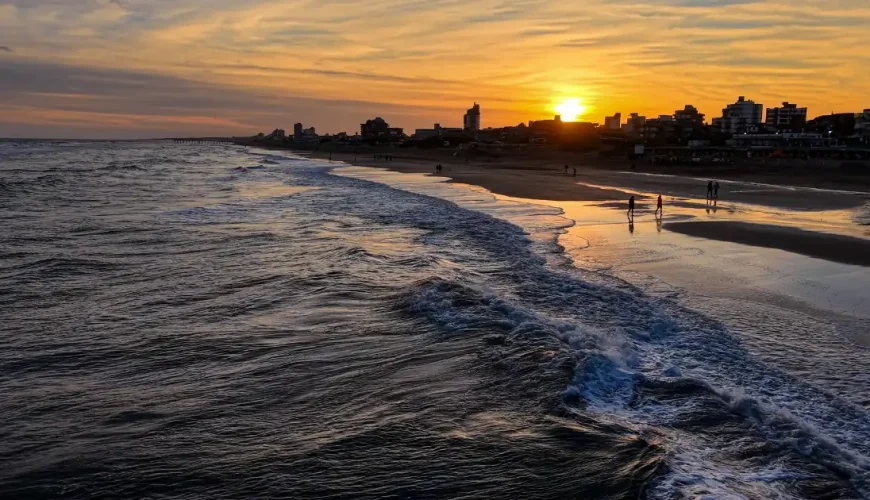 Tramonto su una spiaggia di sabbia con le onde che si infrangono e la sagoma di una città sulla riva