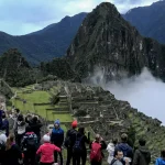 Visitatori che fotografano la cittadella di Machu Picchu e Huayna Picchu sotto una coltre di nuvole basse