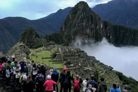 Visitors photographing the Machu Picchu citadel and Huayna Picchu under low cloud