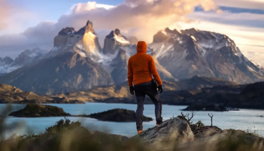 Excursionista con chaqueta naranja frente a los Cuernos del Paine, sobre un lago de color turquesa, en las Torres del Paine, en la Patagonia chilena