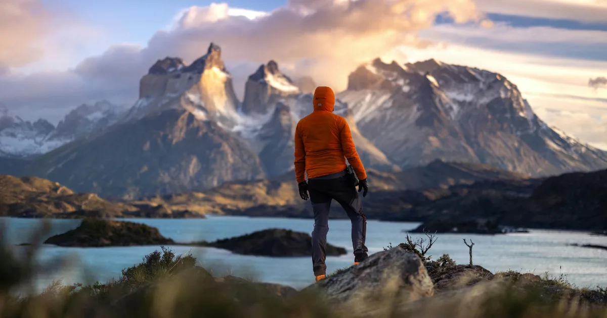 Escursionista con una giacca arancione di fronte ai Cuernos del Paine, sopra un lago turchese, Torres del Paine, Patagonia cilena
