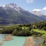 Ein türkisfarbener Gletscherfluss, der sich durch ein grünes Tal unterhalb schneebedeckter Gipfel schlängelt, chilenisches Patagonien