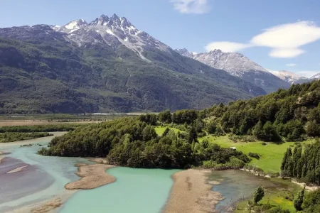 Une rivière glaciaire aux eaux turquoise serpentant à travers une vallée verdoyante, au pied de sommets enneigés, en Patagonie chilienne