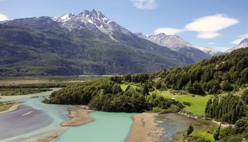 Un río glacial de aguas turquesas que serpentea por un valle verde bajo picos nevados, en la Patagonia chilena