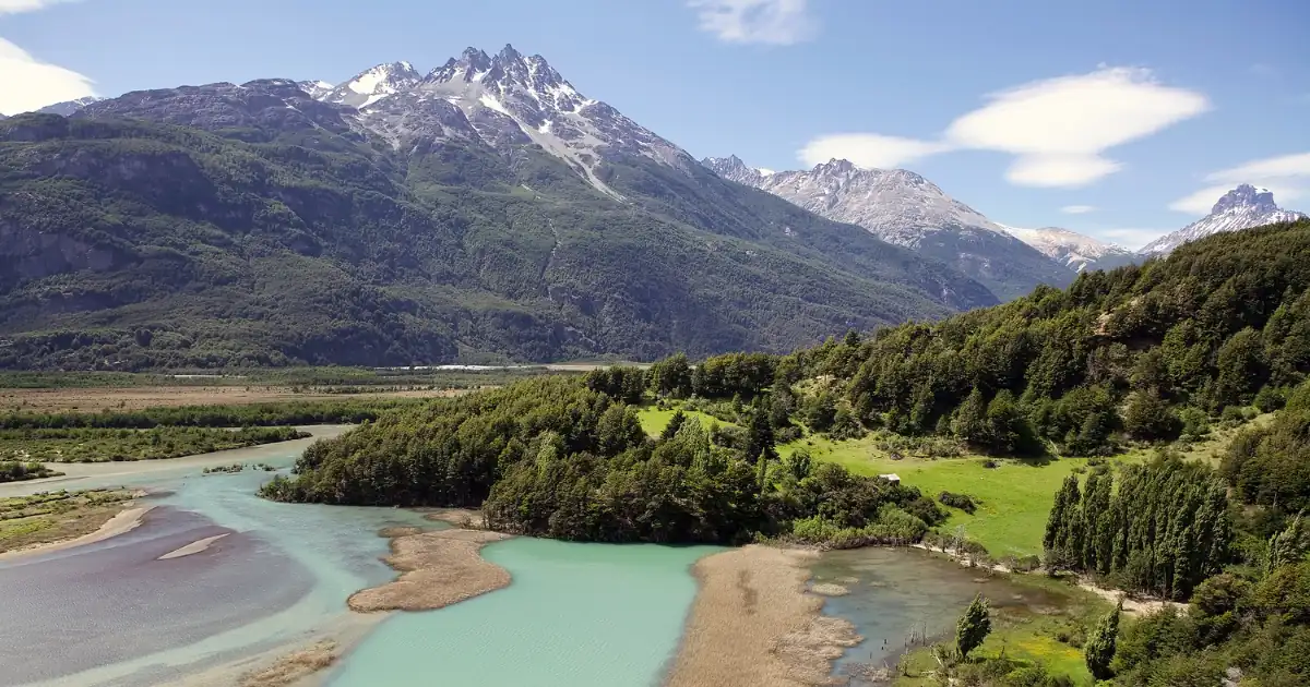 Une rivière glaciaire aux eaux turquoise serpentant à travers une vallée verdoyante, au pied de sommets enneigés, en Patagonie chilienne