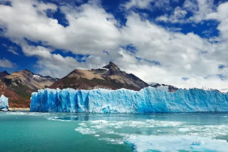 Blue ice wall of a glacier ending in a turquoise lake below brown mountains, Los Glaciares National Park, Santa Cruz, Argentina