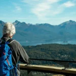 Viaggiatore anziano con uno zaino in spalla presso un belvedere affacciato su un lago nelle Ande, in Patagonia, Argentina