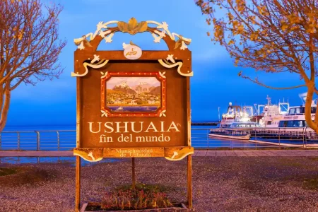 Ushuaia fin del mundo sign beside the harbour at dusk, with tour boats moored behind, Tierra del Fuego, Argentina