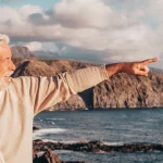 Coppia di anziani che sorride e indica una costa rocciosa e il mare nella calda luce della sera